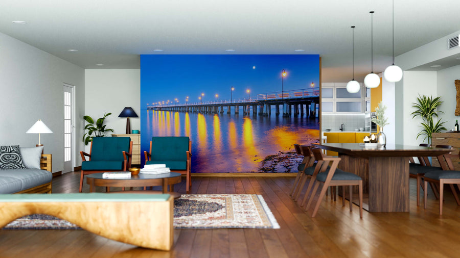 A modern open living-dining room features wooden floors, mid-century furniture, pendant lights, and the Baltic Pier Wall Mural—a stunning depiction of a pier at dusk that creates a spacious, bright, and cozy atmosphere.