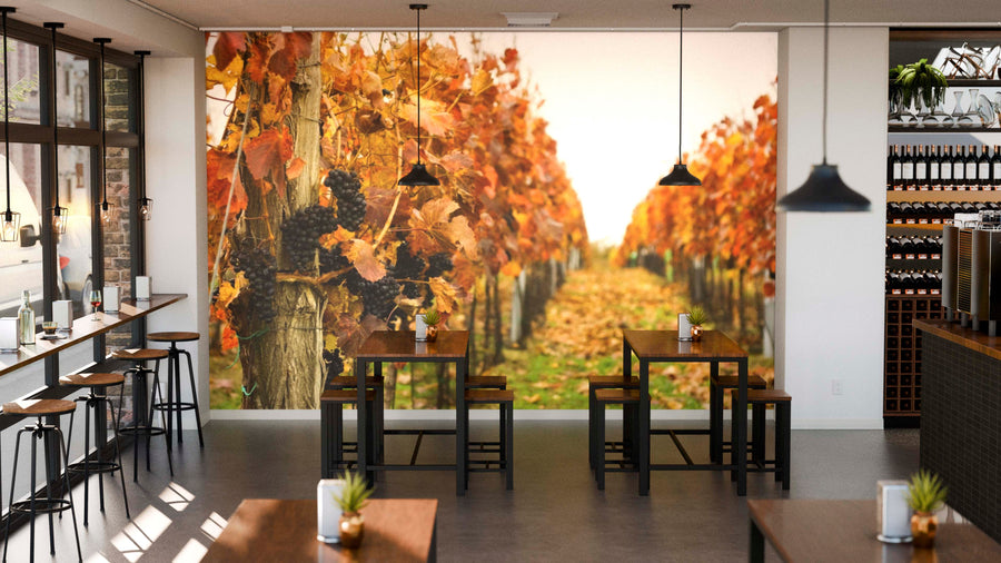 A modern cafe interior features wooden tables, black chairs, hanging lights, and a large Autumn Vineyard Wall Mural, filling the space with warmth as sunlight filters in for an inviting atmosphere.