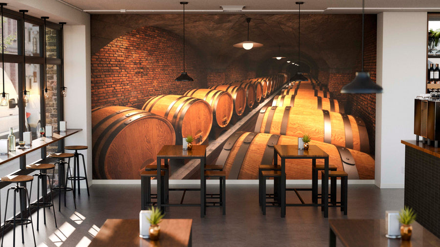 A modern cafe with wooden tables and high stools features the "Barrels in Cellar Wall Mural," exposed brick walls, pendant lights, and small plants on tables, creating a cozy atmosphere.