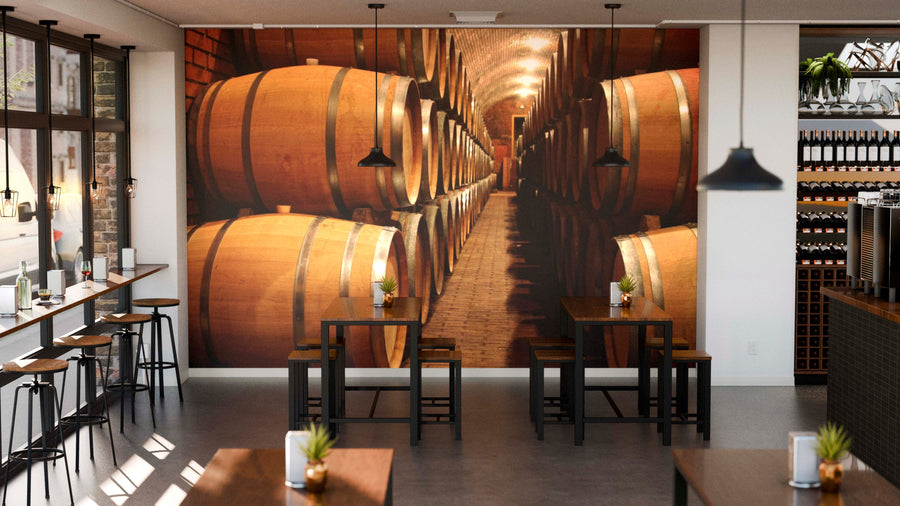 Modern cafe interior with wooden tables and stools. The Barrels in a Winery Wall Mural adds depth, while pendant lights hang above. Natural light fills the space, and shelves with bottles line the right wall.