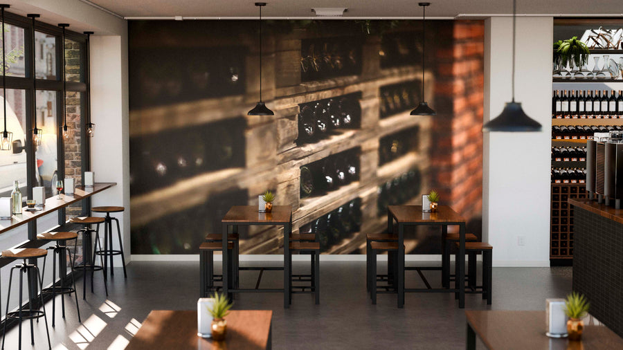 Modern café interior with large windows, wooden tables and stools, small potted plants on each table, and a Bottle Storage Wall Mural covering one wall. Pendant lights hang from the ceiling and shelves with bottles are visible on the right.