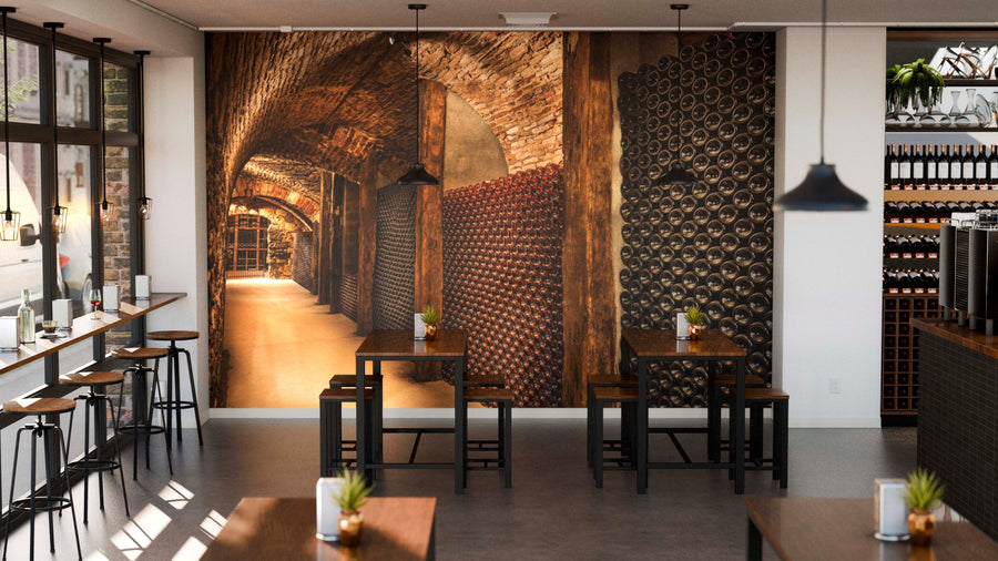 A cozy café with wooden tables, black chairs, potted plants, and pendant lights features a Champagne Bottles Wall Mural that brings warmth and character to the modern space, creating an inviting and unique ambiance.