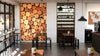 Modern wine bar interior with wooden tables and stools, minimal decor, and a striking Collection of Wine Corks Wall Mural. Large windows fill the space with natural light, while hanging glassware adds a charming touch.