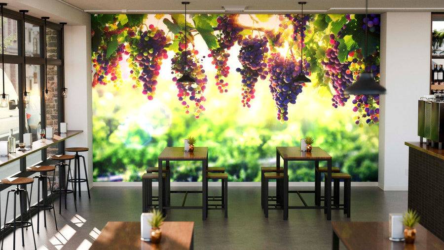 Modern café with wooden tables and black chairs. A bright Colorful Grapes Hanging Wall Mural featuring purple grapes and green leaves covers the back wall, creating a vibrant feel. Potted plants decorate tables; large windows line the left side.