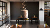 A modern restaurant with wooden tables, black chairs, and pendant lights features a Corkscrew Wall Mural showing a cork being pulled. Wine bottles line shelves on the right.