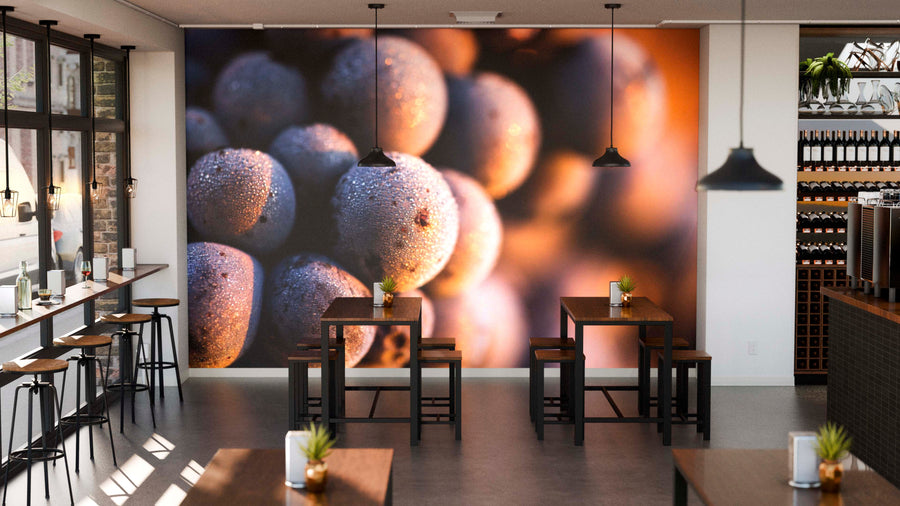 A modern café with wooden tables, black chairs, and pendant lights. The back wall displays the Dew-Covered Purple Grapes Wall Mural. Windows line the left, a wine rack is on the right, and small plants decorate each table.