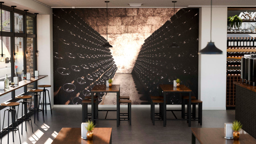 Modern cafe interior featuring the Drinking Bottles Wall Mural depicting a wine cellar. Wooden tables with plant centerpieces, pendant lights above, and large windows fill the space with natural light.