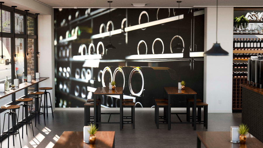 Modern café interior with wooden tables, potted plants, and large windows. A Modern Wine Rack Wall Mural of stacked wine bottles adds character, while pendant lights hang from the ceiling and wine shelves line the right wall.