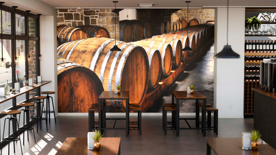 Modern café interior with wooden tables and high stools. The Row of Wooden Wine Barrels Wall Mural adds rustic charm, while sunlight through large windows and potted plants on tables create a cozy, inviting atmosphere.