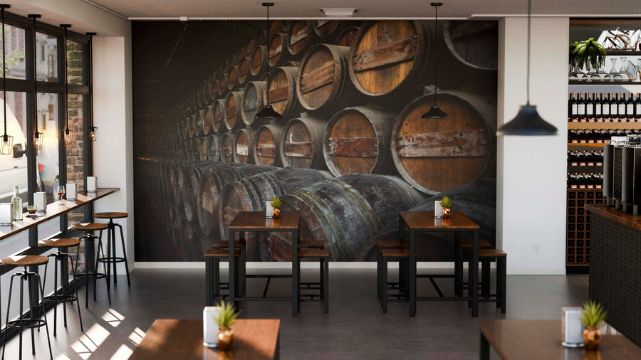 A modern café with wooden tables and stools, small potted plants as centerpieces, and a large Stacked Wine Barrels Wall Mural. Sunlight streams through big windows, while wine bottles are displayed on shelves to the right.
