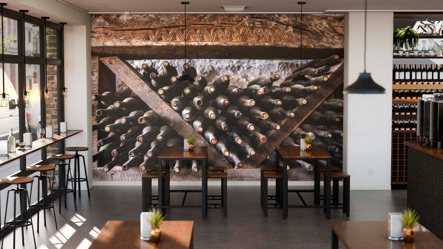Modern café interior featuring wooden tables, stools, large left-side windows, and a "Wine Bottles Covered in Dust Wall Mural." Soft lighting and small potted plants on tables create a cozy, inviting atmosphere.