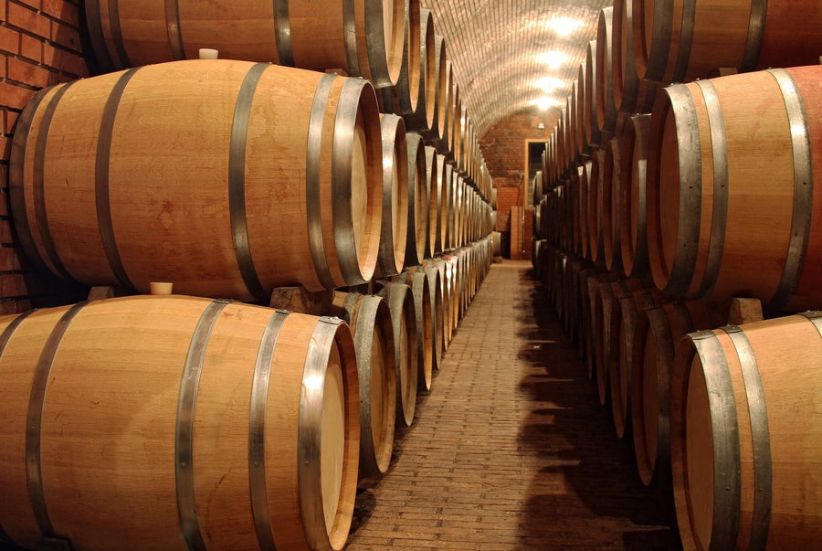 Modern cafe interior with wooden tables and stools. The Barrels in a Winery Wall Mural adds depth, while pendant lights hang above. Natural light fills the space, and shelves with bottles line the right wall.