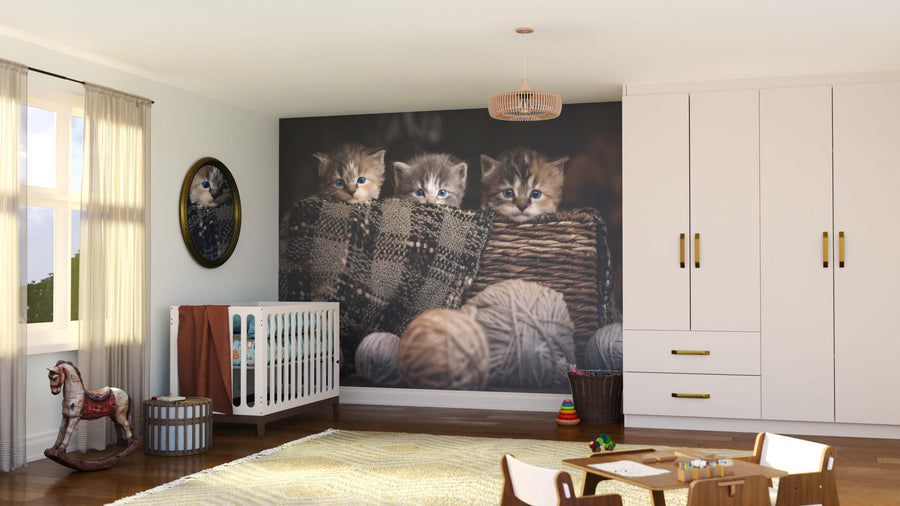 A cozy nursery features the Basket of Cuteness Wall Mural with three kittens, plus a white crib, rug, toys, rocking horse, dresser, and a cat portrait mirror—all bathed in natural light.