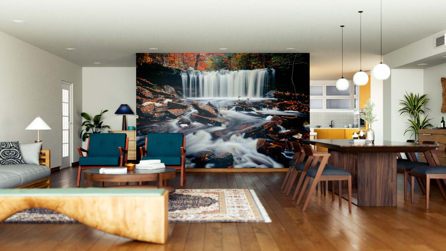 A modern living and dining area with wooden floors, blue chairs, pendant lights, a patterned rug, and an open kitchen with yellow cabinets features the Beautiful Autumn Waterfalls Wall Mural. Natural light fills the spacious, stylish room.