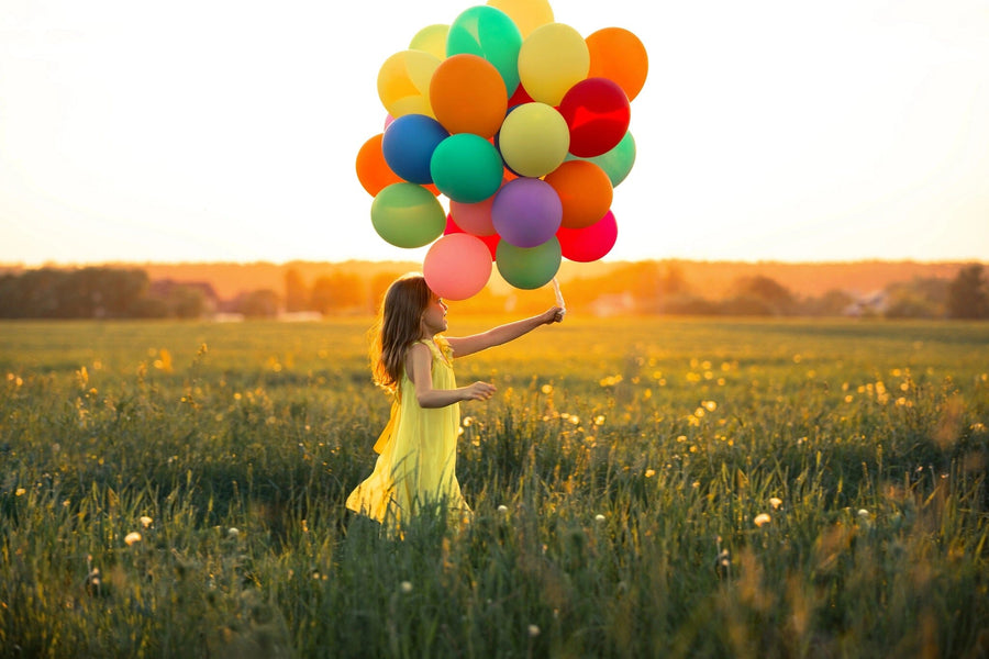 A modern open-plan living and dining room with wood floors features the Beautiful Girl in a Field Wall Mural, showing a girl in a yellow dress holding balloons at sunset, adding vibrant, playful flair to the space.