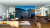 Modern open-plan living and dining room with wood floors and mid-century furniture, featuring the Between Peaks Wall Mural of a serene lake and mountains. Kitchen area visible in the background.