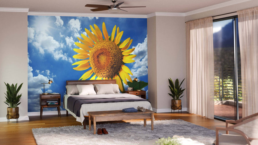 A modern living-dining room with wooden floors and mid-century furniture features the Blue Sky and Sunflower Wall Mural, a peel-and-stick design displaying a large sunflower against blue sky, adding vibrant color. The kitchen is visible in the background.
