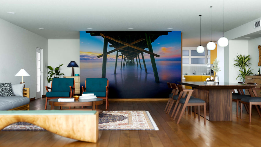 Modern open-plan living and dining area with wood floors, navy and wooden furniture, pendant lights, and a feature wall featuring the Bogue Inlet Pier Wall Mural at sunset for a tranquil beach vibe—perfect for displaying removable wallpaper styles.