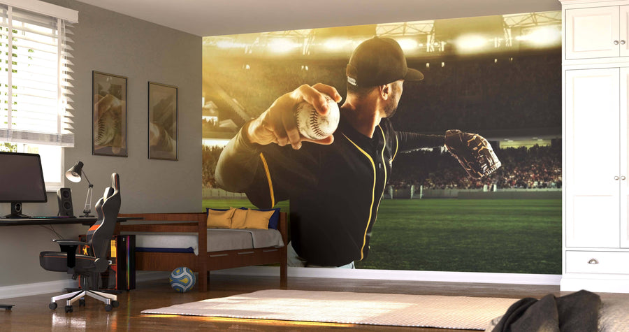 A bedroom features the About to Pitch Wall Mural, showing a baseball pitcher mid-throw in a stadium. The room includes a desk, chair, bed, two sports pictures, a basketball, white cabinets, and sunlight streaming through window blinds.