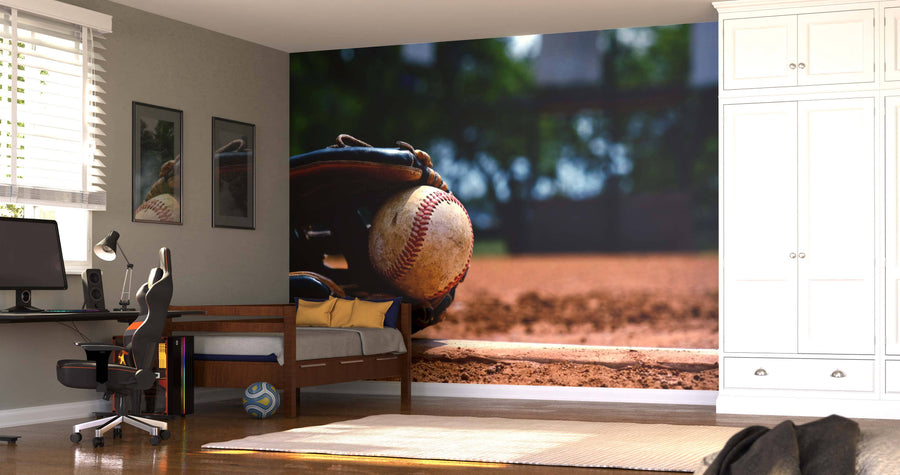 A modern bedroom features the Baseball on the Mound Wall Mural, showing a baseball and glove on a dirt field. The room also has a bed, desk with computer, chair, framed art, blinds on the window, soccer ball on the floor, and white cabinets.