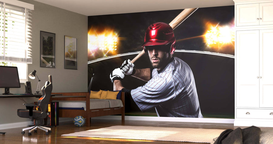 A modern bedroom features the Batter Under Lights Wall Mural, showing a focused baseball player in a striped jersey and red helmet with stadium lights behind. The room also includes a bed, desk, chair, wall art, and soccer ball on the wooden floor.
