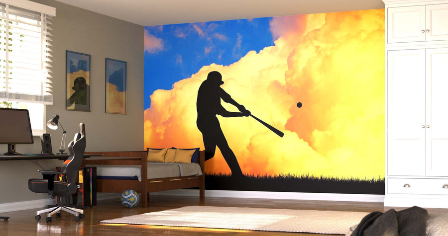 A bedroom showcases the vibrant Batter at Dusk Wall Mural, depicting a baseball player swinging against an orange cloud and blue sky. Sunlight fills the modern space, highlighting its bed, desk, computer, closet, and sleek décor.