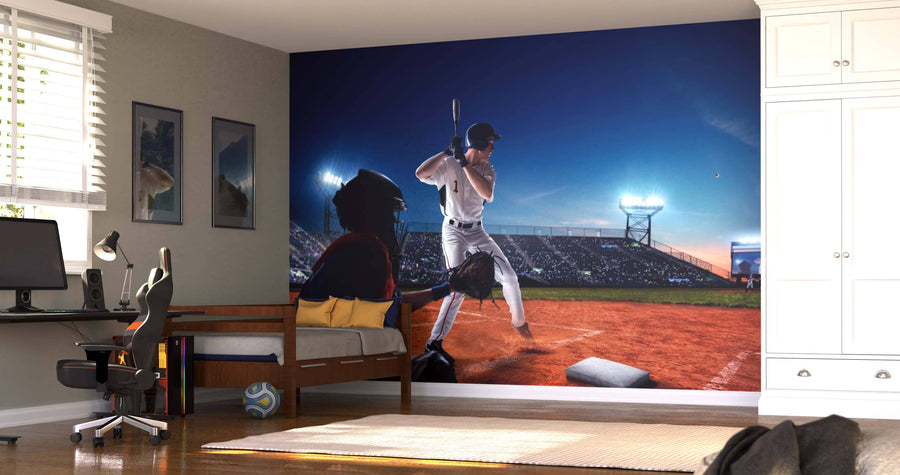 A bedroom features the Batter On-Deck Wall Mural with a baseball batter and catcher at a stadium. The room includes a bed, desk with computer, chair, wall art, sunlight through blinds, and a soccer ball on the wooden floor near the bed.