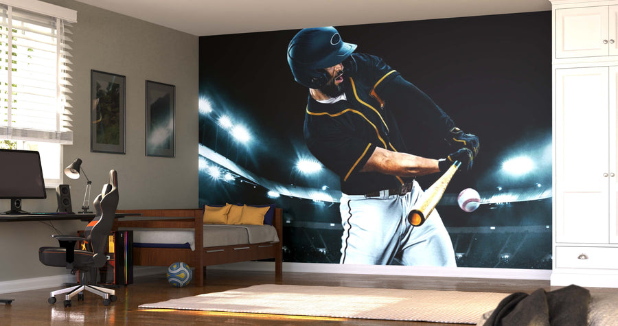 A modern bedroom showcases the Big Swing Wall Mural, a peel and stick mural of a baseball player mid-swing in a stadium. The space includes a desk, chair, bed, white storage cabinets, a soccer ball on the floor, and warm natural light.