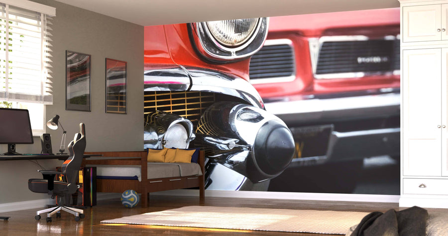A modern bedroom with a desk, computer, bed, and white cabinets features the Classic Cars Wall Mural showing red car grilles and chrome bumpers. Sunlight streams through blinds while a soccer ball rests on the wooden floor.