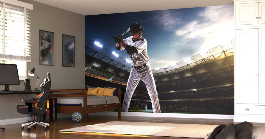 A bedroom with a bed, chair, desk, white wardrobe, window blinds, and sports decor features the Ready to Bat Wall Mural―a large peel and stick mural of a baseball player in uniform preparing to bat in a stadium.