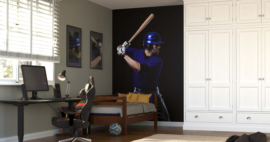 A modern bedroom features the Ready to Hit Wall Mural, showcasing a baseball player in a batting stance behind the bed. Nearby are a desk with a computer and lamp, white cabinets, and sunlight pouring in through the window.