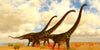 Three large Brachiosaurus with brown skin and green markings walk on a sandy, dry landscape with sparse orange and green plants under a partly cloudy sky—perfect for the Brachiosaurus on Shore Wall Mural.