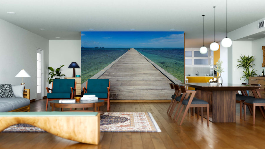 Modern open-plan living and dining room with wood floors, blue and wood furniture, and the "Bridge to the Sea Wall Mural," featuring a wooden dock stretching into a blue ocean for depth and a relaxing coastal vibe.