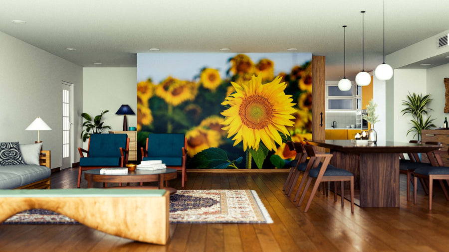A modern living and dining area with wooden floors, dark blue chairs, and a Bright Yellow Petals Wall Mural. The space features pendant lights, a wooden dining table, rugs, houseplants, and an open kitchen in the background.