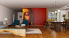 Modern living and dining room with wooden floors, teal armchairs, a gray sofa, and a striking Buddha Face with Red Background Wall Mural. Pendant lights illuminate the dining table, complemented by a cozy rug and coffee table.