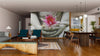 A modern living-dining room with wood floors, green and wood furniture, pendant lights, rugs, and an open kitchen features the Buddha Hands Holding Flower Wall Mural depicting a lotus flower in statue hands as a striking focal point.