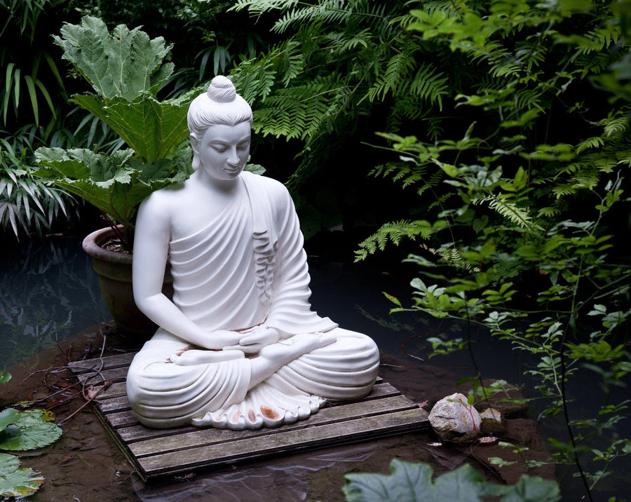 A modern living-dining room with wood floors and cozy seating is enhanced by the Buddha Statue in Pond Wall Mural, showcasing a serene white Buddha in a green garden, and complemented by pendant lights and decorative rugs.