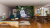 A modern living-dining room with wood floors and cozy seating is enhanced by the Buddha Statue in Pond Wall Mural, showcasing a serene white Buddha in a green garden, and complemented by pendant lights and decorative rugs.