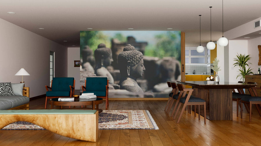 A modern open-plan living and dining room features wooden floors, teal chairs, a wood dining set, warm lighting, and a large Buddhas in Indonesia Wall Mural as a striking feature wall, with the kitchen area visible in the background.