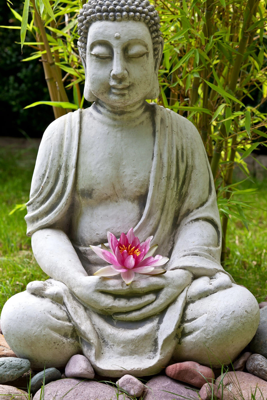 A serene living room showcases the "Buddha with Lotus and Bamboo Leaves Wall Mural," featuring a stone Buddha statue, pink lotus, and bamboo. Modern wooden furniture and green walls complete the peaceful, zen-inspired space.