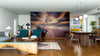 A modern living and dining area features wooden floors, stylish furniture, pendant lights, and the Calm Ocean Walkway Wall Mural—a striking peel and stick mural of a dock stretching into a tranquil lake at sunset with vibrant clouds.