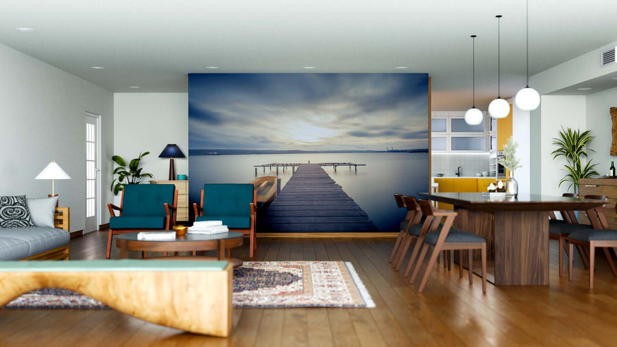 A modern living and dining area with wooden floors, teal chairs, a sofa, and the Calm Waters at Sunset Wall Mural featuring a pier into a serene lake. Plants, pendant lights, and a rug add warmth to this stylish open space.