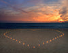 The Candles Heart Wall Mural by Deposit Photo depicts lit candles forming a heart on a sandy beach at sunset, with the orange and pink hues of the sky mirrored in the tranquil ocean, creating a romantic and peaceful atmosphere.