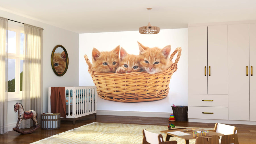 A bright nursery features a crib, toys, mirror, and the Cats in a Basket Wall Mural displaying three orange kittens in a wicker basket. Light streams through the window and a soft rug adds warmth to the wooden floor.