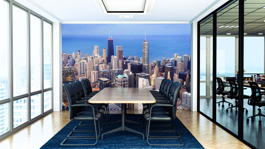 A bright, modern conference room with a long wooden table and black chairs features the Chicago Aerial View Hancock Building Wall Mural of a city skyline under blue skies; the adjacent room is visible through glass walls.