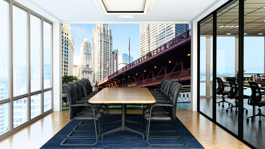 A modern conference room features a long wooden table, black chairs, and the Chicago Du Sable Bridge Wall Mural showing a cityscape. Glass walls reveal another office area, while sunlight streams in through large windows.