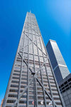 A low-angle view of a skyscraper with a crisscrossed steel framework and reflective glass windows against a clear blue sky. A neighboring building is visible, offering inspiration for the Chicago John Hancock Building Wall Mural, capturing height and modern architectural style.