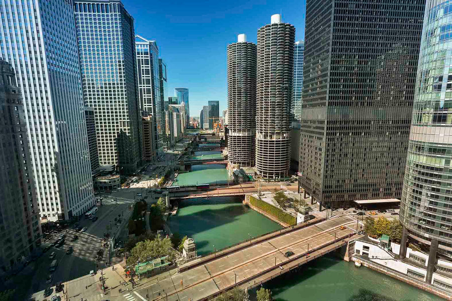 A modern conference room features a long wooden table, eight black chairs, glass walls, and a Chicago River Marina Towers Wall Mural. Natural light fills the space with another office visible through the glass.