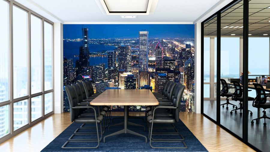 A modern conference room with black chairs and a long wooden table features the "Chicago Skyscrapers Aerial View at Night Wall Mural"; a blue rug lies beneath, and glass walls reveal another office area.