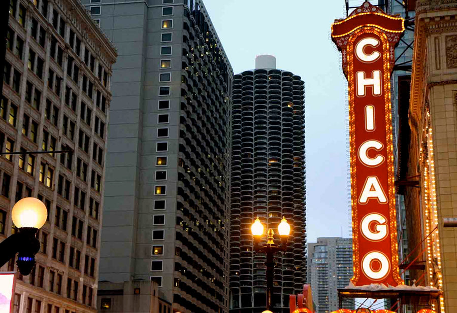 A modern conference room with black chairs around a long wooden table features floor-to-ceiling windows, city views, and one wall covered by the Chicago Theater Sign Wall Mural. Glass walls separate it from adjacent offices.